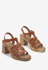 Sandales à talons en cuir marron avec plusieurs brides verticales, boucle de cheville et un talon en bois texturé. Semelle lisse et couture décorative minimaliste.
