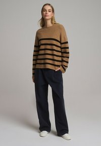 Brązowy sweter w paski z miękkiego materiału, z czarnymi paskami. Zestawiony z luźnymi, ciemnymi spodniami i białymi butami na slip-on.