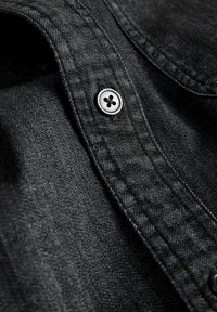 Primo piano di tessuto denim nero con un bottone metallico cucito su una patta cucita di un indumento.