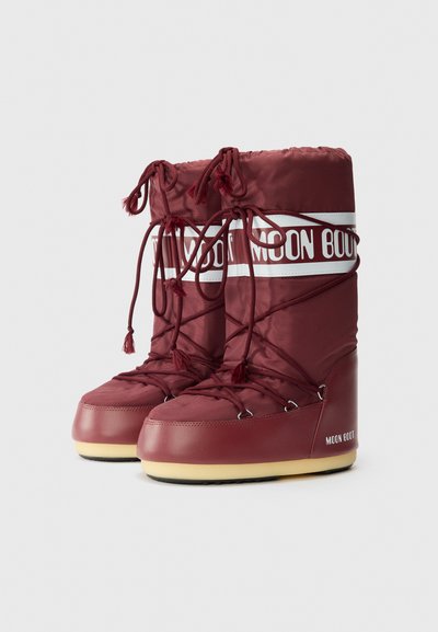 Botas de nieve marrón púrpura con un acabado brillante, que cuentan con la marca blanca, cordones ajustables y una suela texturizada para mayor tracción.