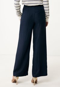 Marineblauwe wijduitlopende broek van een gestructureerde stof, met een hoge taille, plooien en een achterzak, gecombineerd met beige hakken.