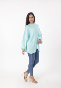 Hellblauer, übergroßer Pullover mit Rundhalsausschnitt, gerippten Bündchen und strukturierter Oberfläche, kombiniert mit eng anliegenden Jeans und transparenten Sandalen mit Absatz.