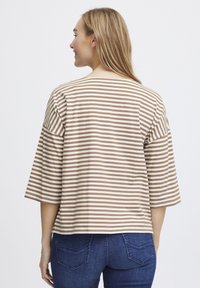 Top a righe in beige e bianco, con maniche ampie e una vestibilità rilassata e cropped. Tessuto liscio con una leggera lucentezza.