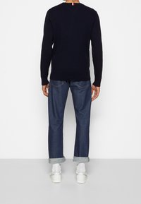 Pull côtelé bleu marine à manches longues, avec un col en V dans le dos. Assorti à un jean foncé retroussé et des chaussures blanches à enfiler.