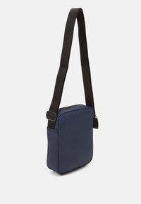 Bolso cruzado de color navy hecho de un material suave con forma rectangular, que cuenta con una correa negra ajustable y un cierre superior con cremallera.