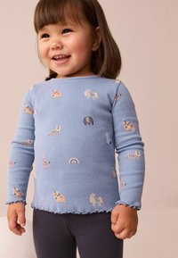 Hellblau gestreiftes Langarmshirt mit bunten Tiermustern und einem Rüschensaum. Kombiniert mit dunklen Leggings.