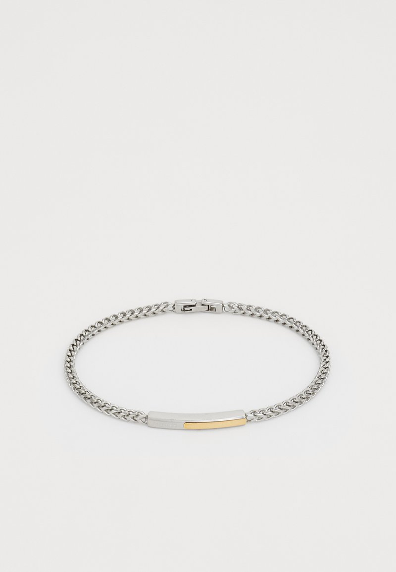 Bracelet en chaîne argentée avec une barre rectangulaire mettant en valeur un accent doré et un fermoir sécurisé sur fond blanc.