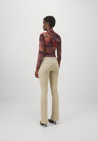 Haut à manches longues à motifs dans des couleurs chaudes, associé à un pantalon évasé beige clair. Le tissu semble lisse avec un design moulant.