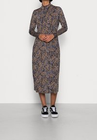 Abito attillato a maniche lunghe con stampa leopardata blu e marrone, realizzato in tessuto morbido; abbinato a sneakers in bianco e nero.