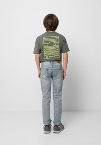 Camiseta gris con un gran gráfico de un atardecer amarillo en la espalda, combinada con jeans azul claro y zapatillas grises. Estilo clásico y casual.