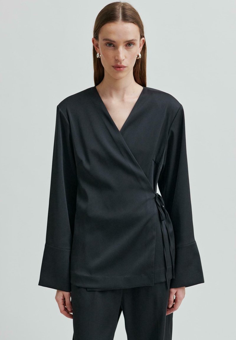 Černý top s dlouhými zvonovými rukávy v hladké tkanině, s detailním zavazováním na boku. Jednoduchý, moderní design s výstřihem ve tvaru V.