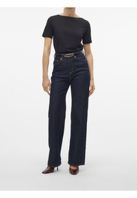 Czarny t-shirt z krótkim rękawem, ciemnoniebieskie dżinsy z wysokim stanem i szerokimi nogawkami ze złotymi dodatkami, zestawione z ciemnobrązowymi butami na obcasie.