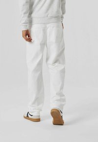 White denim jeans with a relaxed fit, featuring two back pockets and subtle stitching details, paired with black and white sneakers.