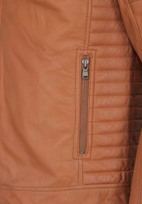 Beige Lederjacke mit einem Reißverschlussfach, gestepptem Muster an der Seite und glatter Oberfläche, die ihr elegantes Design und ihre Funktionalität betont.