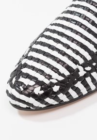 Chaussure en cuir tressé avec un bout pointu, présentant des bandes alternées noires et blanches, et une texture lisse.