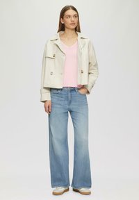 Leichtgewichtige beige cropped Jacke mit großen Knöpfen, einem rosa V-Ausschnitt-Pullover und weit geschnittenen hellblauen Jeans; das Schuhwerk hat eine cremefarbene Basis und eine sandfarbene Sohle.