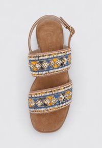 Sandalia con cuentas que presenta dos correas anchas con un patrón en azul, amarillo y blanco, montada sobre una plantilla de gamuza marrón y con una hebilla ajustable.