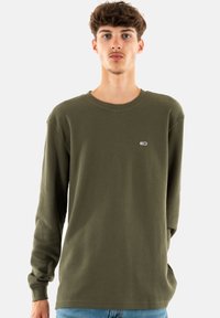 Camisa de manga larga verde oliva hecha de una tela texturizada con cuello redondo; presenta un pequeño logo en el lado izquierdo del pecho.