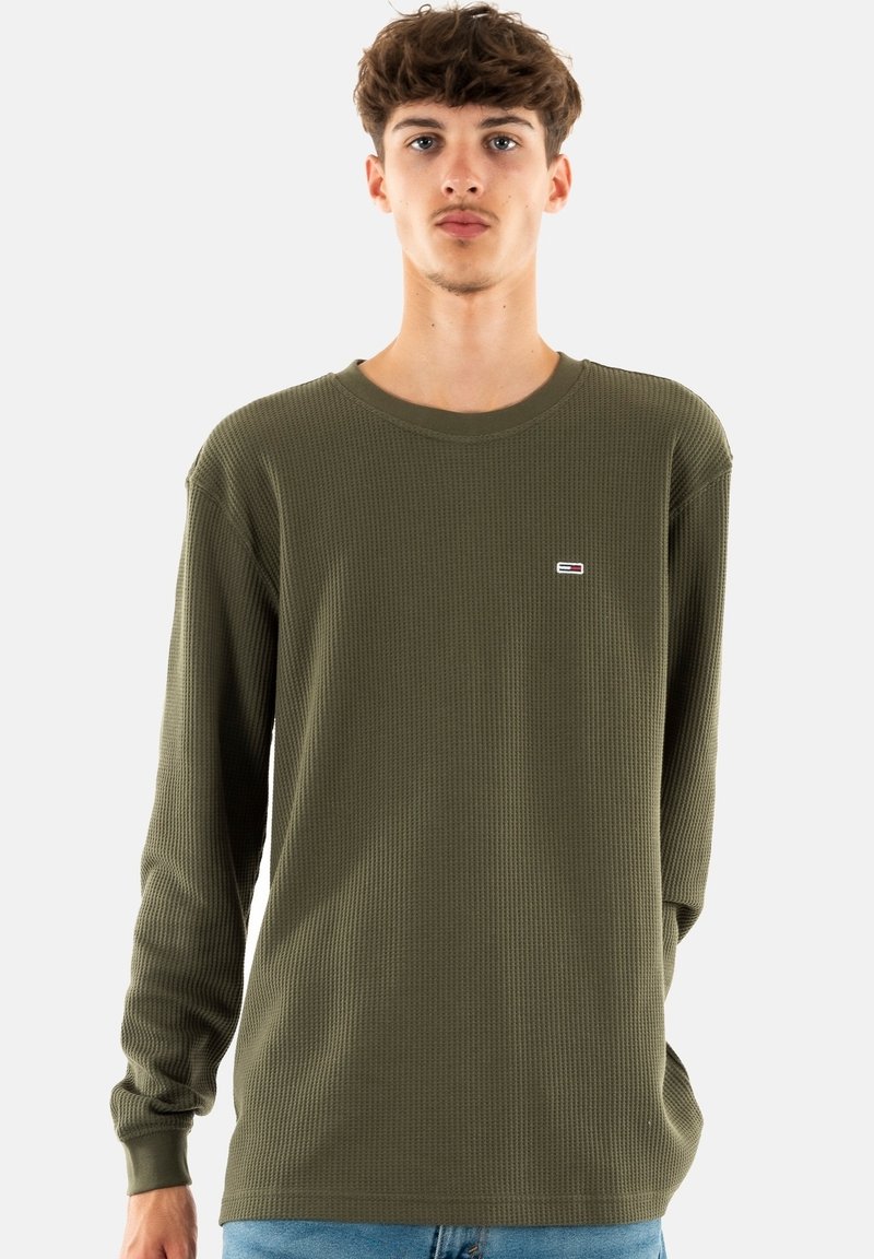 Camisa de manga larga verde oliva hecha de una tela texturizada con cuello redondo; presenta un pequeño logo en el lado izquierdo del pecho.