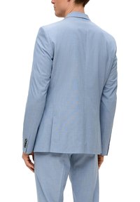 Blazer azzurro chiaro con una texture liscia, vestibilità su misura, spacco singolo e dettagli con quattro bottoni sui polsini. Indossato con pantaloni abbinati.