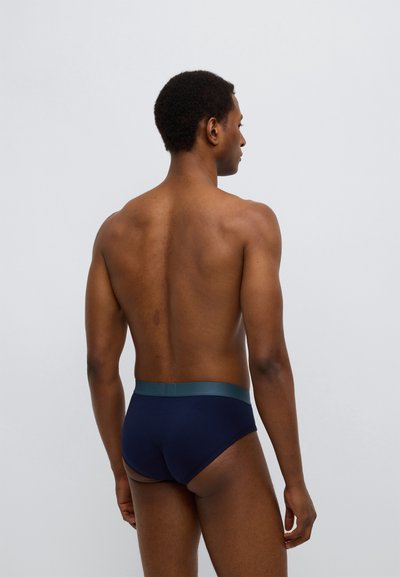 Vyriškos tamsiai mėlynos trumpikės su kontrastine žalia elastine juosmens juosta, pasižyminčios lygiu audinio paviršiumi ir prigludusia forma.