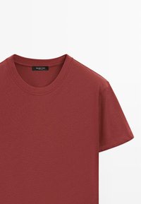 T-shirt à manches courtes et col rond de couleur rouge rouille avec une étiquette noire affichant la marque Massimo Dutti à l'intérieur du col.