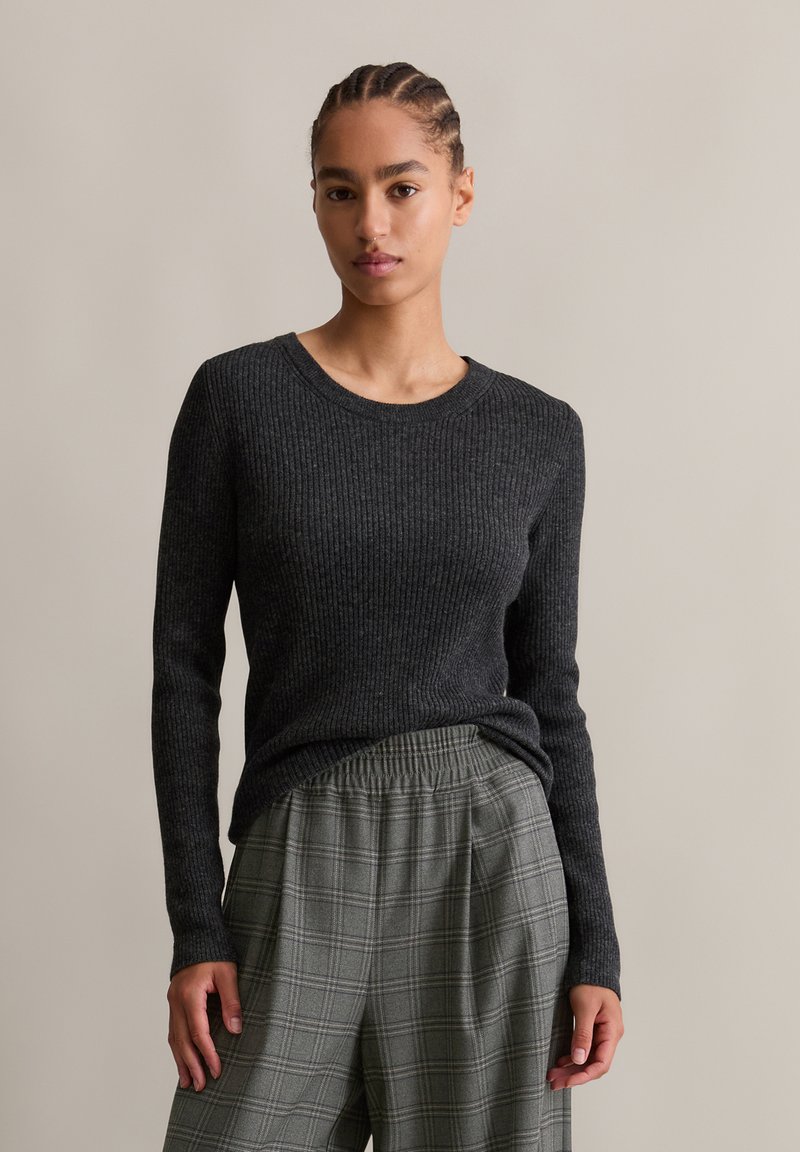 Dunkelgrauer, gerippter Langarmpullover mit Rundhalsausschnitt, kombiniert mit hellgrauen Karo-Hosen mit weitem Bein und elastischem Bund.