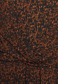 Černá a oranžová látka s měkkou texturou, zdobená vzorem s vráskami a proplétajícími se záhyby.