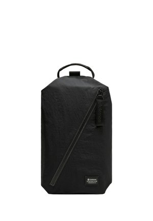 Petite pochette rectangulaire noire avec fermeture éclair diagonale, poignée en tissu en haut, et petite étiquette de marque rectangulaire près du bas.