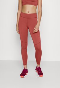 Leggings a coste, a vita alta, di un colore rosa tenue con pannelli laterali in contrasto, abbinati a scarpe da ginnastica color bordeaux con accenti luminosi.