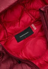 Red insulated jacket interior featuring quilted texture, black brand label reading "PeakPerformance," and a size tag labeled "S."