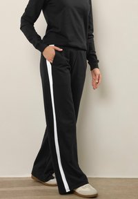 Svarta sweatpants med en vit sidremsa, med avslappnad passform och fickor. I kombination med en svart långärmad topp och ljusa sneakers.