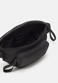 Borsa nera in nylon con scomparto principale con cerniera e tasca frontale. Caratterizzata da un design semplice e una texture liscia. Etichetta del marchio visibile all'interno.
