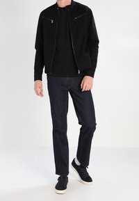 Černá bomber bunda s kapsami na zip, spárovaná s černým tričkem a tmavě modrými džíny. Boty jsou černé s bílou podrážkou.