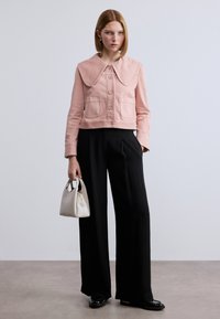 Ροζ cropped σακάκι με μεγάλο γιακά, δύο μπροστινές τσέπες και κουμπιά. Συνδυασμένο με μαύρο παντελόνι φαρδύ στο κάτω μέρος και μικρή λευκή τσάντα χειρός.