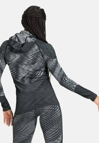 Langarm-Sportoberteil mit Kapuze, das ein schwarz-graues Wellenmuster aufweist, aus leichtem, dehnbarem Stoff gefertigt und für aktive Nutzung konzipiert.