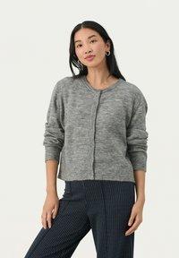 Cardigan gris en tricot avec un col rond, fermeture à boutons, manches longues et poignets côtelés, associé à un pantalon marine à rayures.