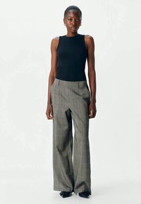 Top de malha preto com riscas, combinado com calças cinzentas de xadrez de cintura alta, apresentando pernas largas e detalhes subtis em vermelho no padrão.