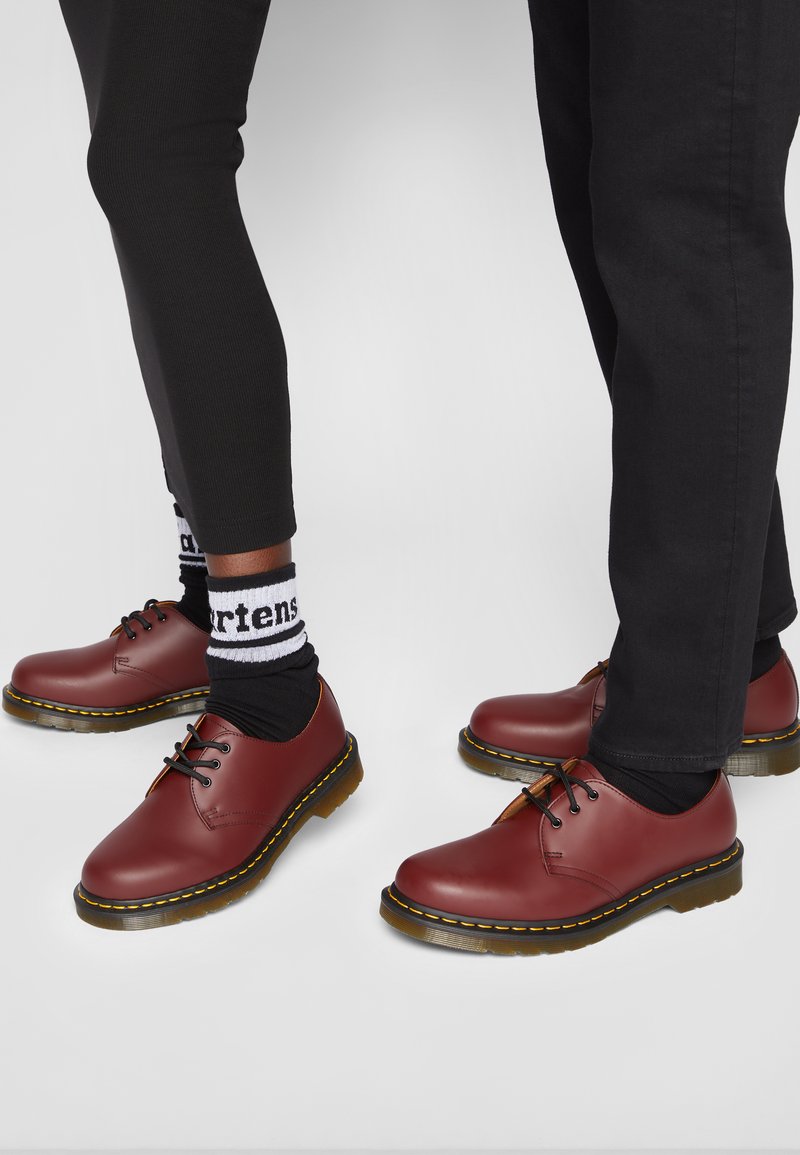 Bruine leren schoenen met een ronde neus, dikke zolen en gele stiksels. Draag met zwarte leggings en gestreepte sokken.