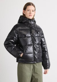 Svart puffjakke med en glanset overflate, hette, glidelås foran og justerbar snøring. Har quiltet tekstur og sidelommer.