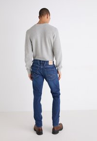 Slim fit, kék farmernadrág, amely denimből készült, egy világosszürke, texturált pulóverrel párosítva. A hátsó részen két zseb és egy márkázott címke található.