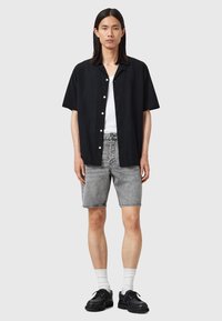 Svart kortärmad skjorta i texturerad tyg, vita knappar, tillsammans med ljusgrå denimshorts och svarta skor, med vita strumpor.