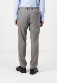 Pantaloni grigi su misura con una finitura testurizzata. Presentano due tasche posteriori con bottoni e un taglio diritto. Indossati con scarpe nere.