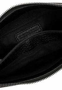 Bolsa de cuero negro con dos compartimentos, que cuenta con un cierre de cremallera y una etiqueta en relieve. La textura de la tela interior es suave con un acabado mate.