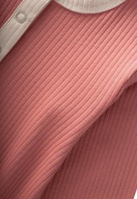 Tuva tuvplānā rozā ribotā auduma ar baltu ribotu apkakli un pogu detaļām uz apģērba.