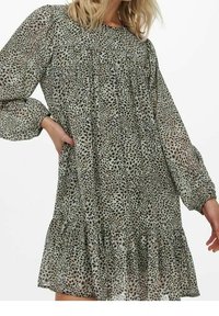 Vestido de estampado de leopardo en tejido ligero, con mangas largas, escote redondeado y un dobladillo de volantes. Los colores incluyen verdes y marrones apagados.