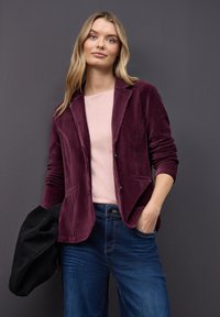 Fløjl blazer i dyb burgunder med en skræddersyet pasform og klapkraver, parret med en lyserød top og mørk denim jeans.