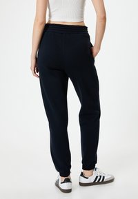 Marine joggerbroeken met een elastische tailleband en boorden; gemaakt van zacht materiaal. In combinatie met witte sneakers met zwarte strepen.