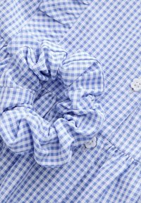 Chouchou en tissu à carreaux bleu clair et blanc placé sur une chemise à carreaux assortie avec des boutons blancs.
