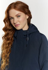Giacca impermeabile navy con cappuccio, dotata di cordini regolabili e una finitura liscia e texturizzata. Design semplice con hardware minimale.